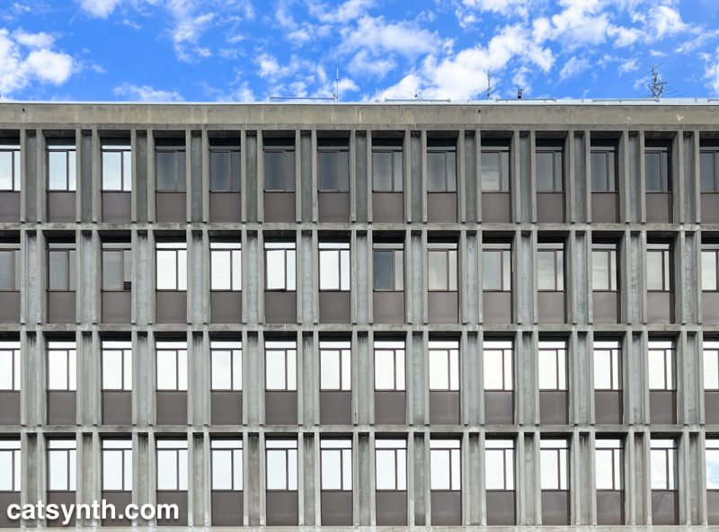 Brutalist building facade with a regular grid-like arrangement of windows, beams, and columns.