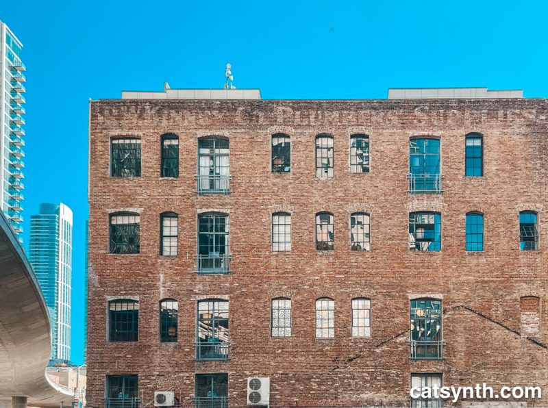 Old brick building with refurbished windows.  To the left is a freeway ramp and two tall glass skyscrapers. The image is artificially colored with extra blue and red.