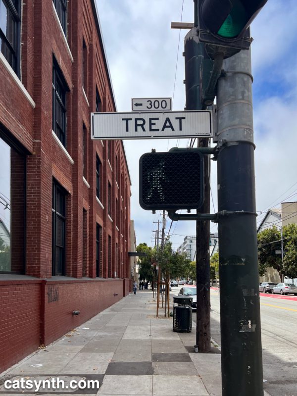 San Francisco street sign for "Treat Avenue" on a post next to a brick building.