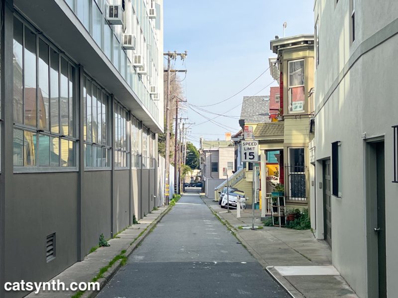 Looking down a narrow alley in San Francisco with a modern building on the left and classic San Francisco houses on the right.  A sign says "Speed Limit 15"