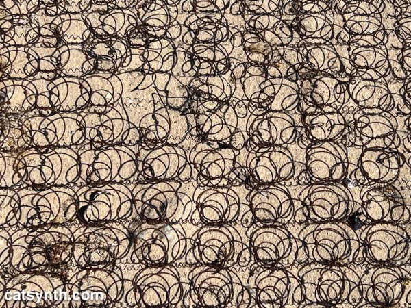 A field of rusted metal coils and their shadows in the sand.