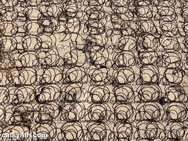 A field of rusted metal coils and their shadows in the sand.