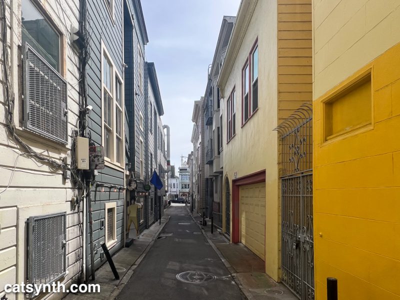 Looking south down a narrow alley. There are older buildings to each side, with the ones on the right being bright yellow.