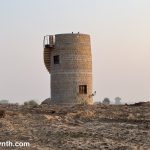 Small cylindrical two-story tower made of sandstone with a spiral staircase on the outside, sitting in a desert landscape.