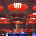 Flat ceiling with round circular modernist light fixtures receding into the distance. On the far wall we see bright blue screens.