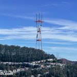 Sutro Tower (giant communications antenna) above a full covered with trees and dotted with houses.